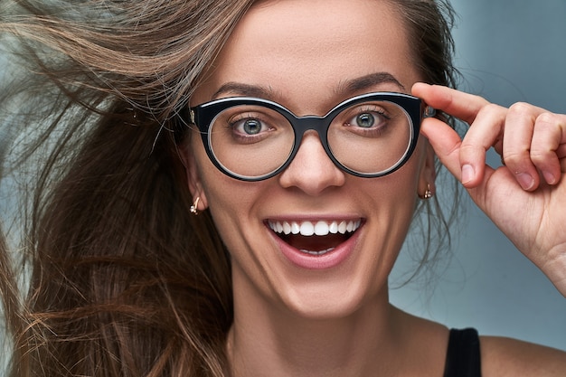 Retrato de joven caucásica morena mujer feliz con sorprendido alegre sorprendido emocionado sorprendido expresión de la cara en gafas de marco negro con la boca abierta de sorpresa. Wow y omg