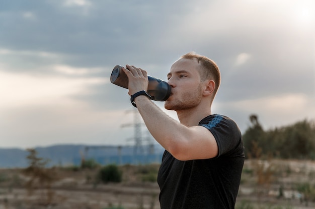 Retrato de un joven caucásico bebiendo agua de una botella después o antes del entrenamiento