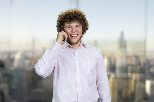 Foto retrato de un joven caucásico con camisa blanca hablando por teléfono en una ventana interior borrosa