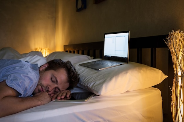 Retrato de un joven caucásico cansado acostado en la cama usando una laptop durante mucho tiempo