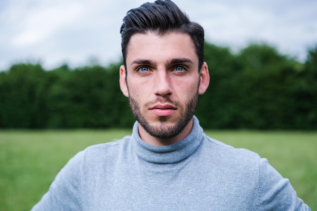 Retrato de un joven caucásico con ojos claros y rostro serio al aire libre en el parque Concepto estilo de vida serio