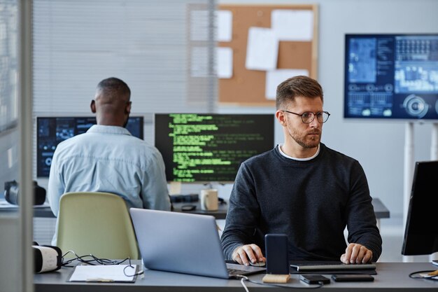 Retrato de un joven caucásico que usa una computadora mientras programa software en el espacio de copia de la oficina