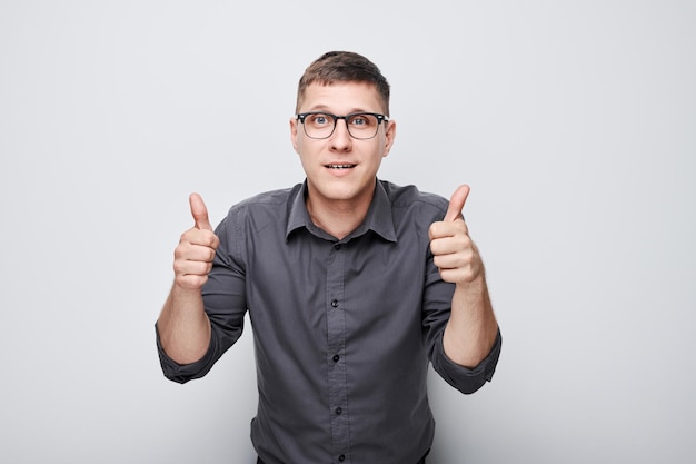 Retrato de un joven caucásico sonriendo alegremente mostrando los pulgares hacia arriba gesto aislado en el fondo blanco del estudio Aprueba la buena elección la decisión correcta