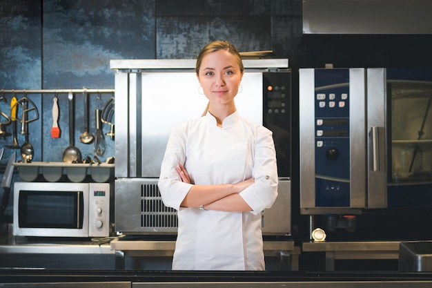 El retrato de una joven chef confiada y sonriente vestida con uniforme blanco de cocina profesional está en el fondo