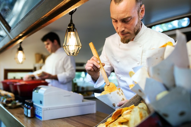 Retrato de joven chef sirviendo patatas a la barbacoa en un camión de comida.