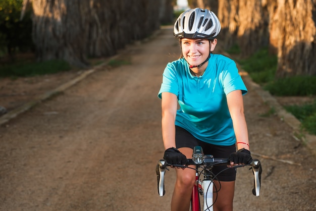 Retrato de joven ciclista femenina en bicicleta en carretera con palmeras