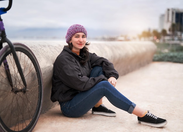 Retrato joven ciclista latina sentada en la calle junto a una bicicleta feliz x9