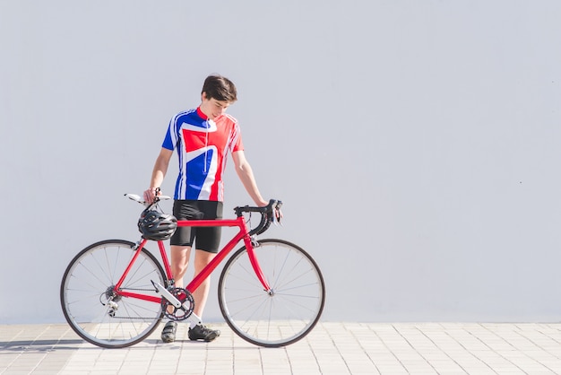 Retrato de un joven ciclista de pie con una bicicleta de carretera roja