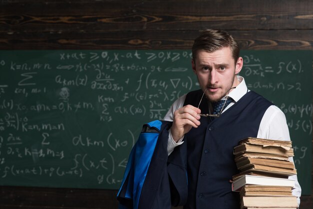 Retrato de un joven confiado con un montón de libros sosteniendo un auricular de sus gafas en la boca