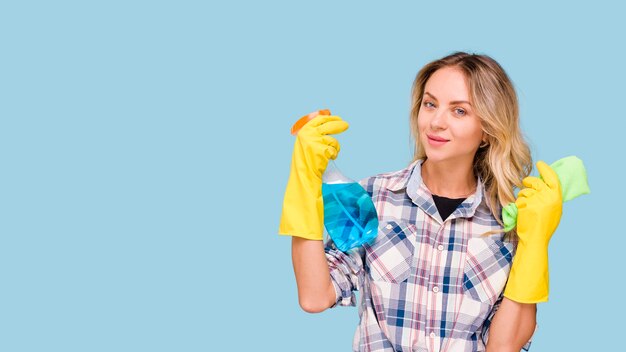 Retrato de joven conserje mujer sosteniendo una botella de spray de detergente y servilleta