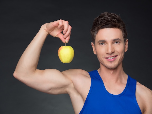 Retrato de joven culturista sonriente sosteniendo manzana en fondo negro.