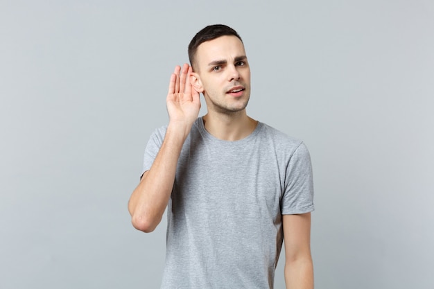 Retrato de joven curioso en ropa casual escuchando mano cerca de la oreja