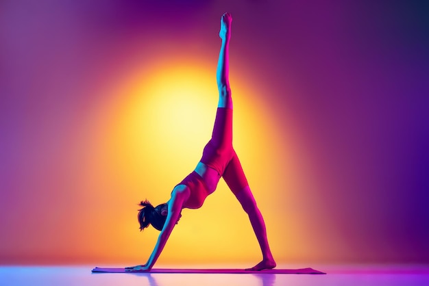 Retrato de una joven deportista haciendo ejercicios de yoga levantando la pierna hacia arriba aislada sobre fondo rosa y amarillo degradado en neón