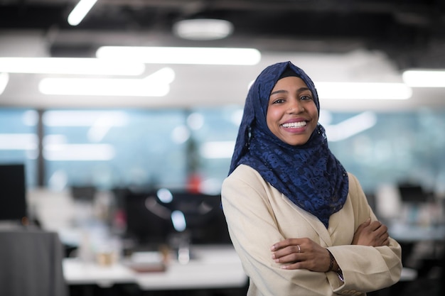 Retrato de joven desarrollador de software femenino afroamericano musulmán con bufanda azul de pie en la oficina de inicio moderno