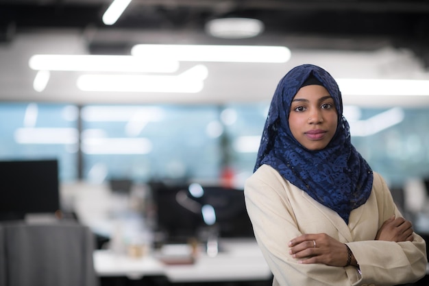 Foto retrato de joven desarrollador de software femenino afroamericano musulmán con bufanda azul de pie en la oficina de inicio moderno