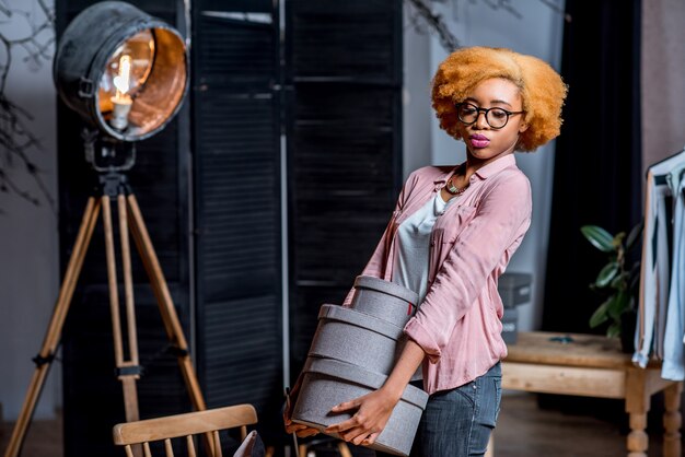 Retrato de un joven diseñador de moda africano hoding cajas en el interior del estudio