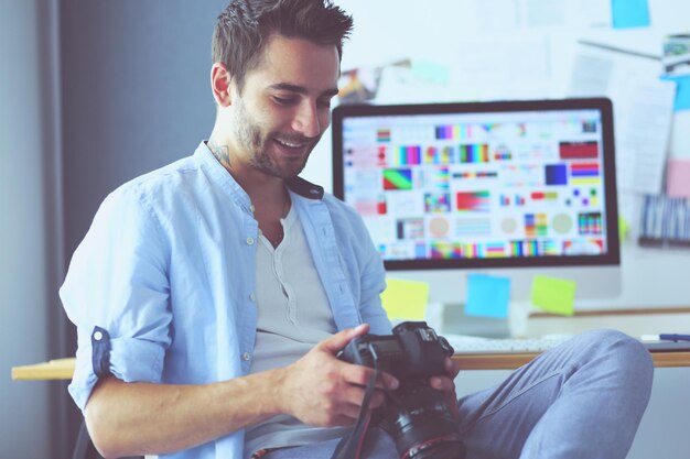 Retrato de un joven diseñador sentado en un estudio gráfico frente a una laptop y una computadora mientras trabaja en línea