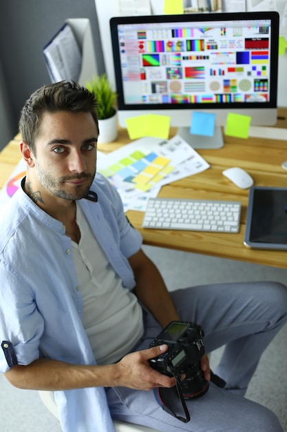 Retrato de una joven diseñadora frente a una computadora portátil y una computadora mientras trabaja Asistente usando su móvil en segundo plano