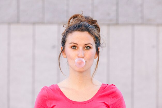 Retrato de una joven divertida que sopla chicle rosa