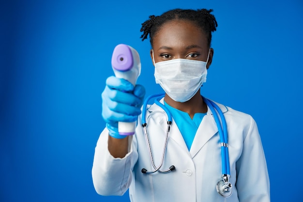 Retrato de una joven doctora africana con máscara médica en un estudio azul