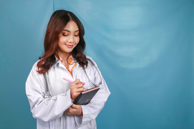 Retrato de una joven doctora asiática, una profesional médica, sonríe y sostiene notas aisladas sobre el fondo azul.