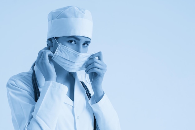 Retrato de una joven doctora poniéndose una mascarilla médica protectora en el espacio de copia de fondo blanco