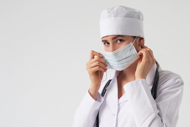 Retrato de joven doctora poniéndose mascarilla médica protectora en la pared blanca, espacio de copia