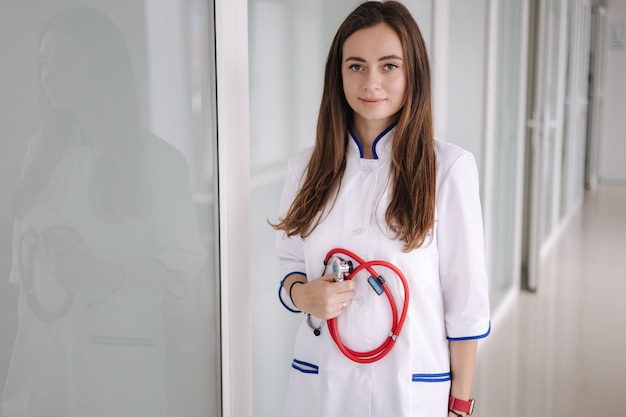 Retrato joven doctora sosteniendo un estetoscopio en manos clínica brillante