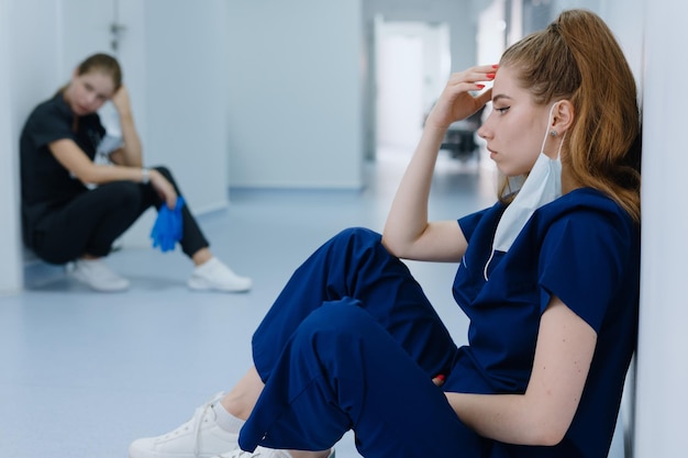 Retrato de una joven doctora con traje azul que está cansada y exhausta sentada en el pasillo del hospital