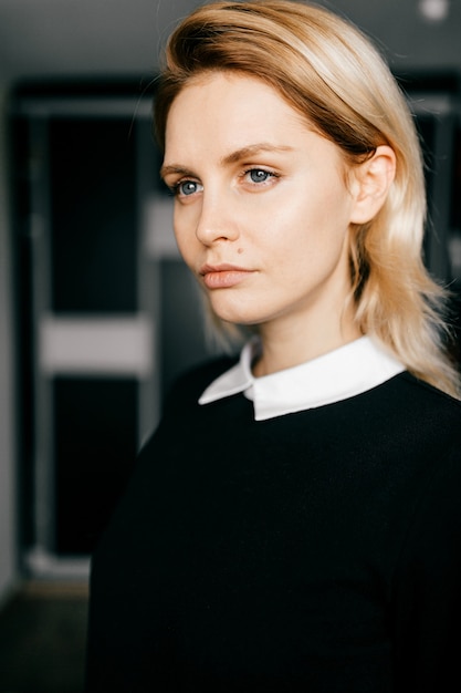 Retrato de joven elegante rubia de pelo corto en ropa formal negra posando en interiores