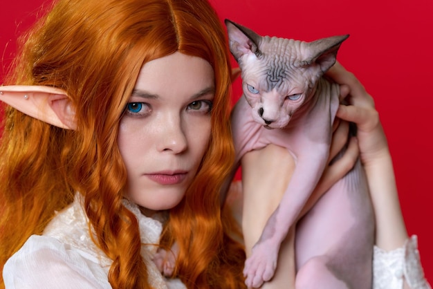 Retrato de una joven elfa cosplayer que muestra un gatito esfinge de pura raza con ojos azules