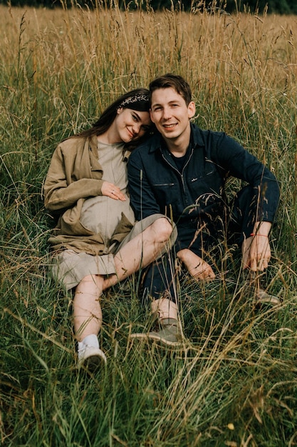 Foto retrato de una joven embarazada sentada con un hombre en un terreno de hierba