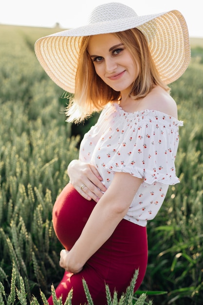 Retrato de joven embarazada con sombrero de paja, caminando en la naturaleza en verano. Atención durante el embarazo. Belleza y salud. Felicidad y serenidad. Estilo de vida saludable. Cosméticos para embarazadas.