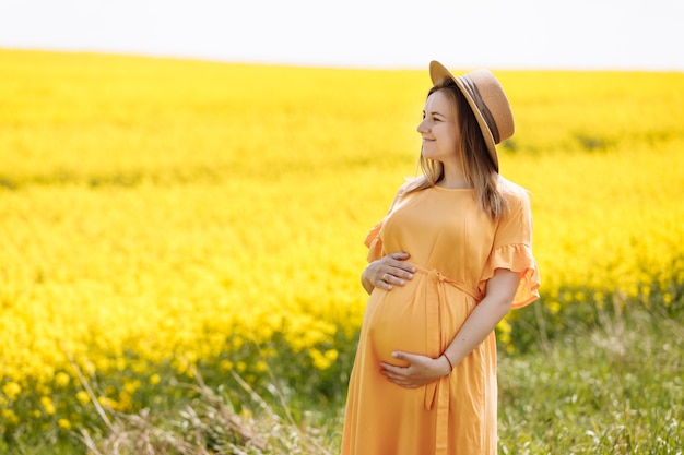 Retrato de una joven embarazada con un sombrero y un vestido amarillo al sol.