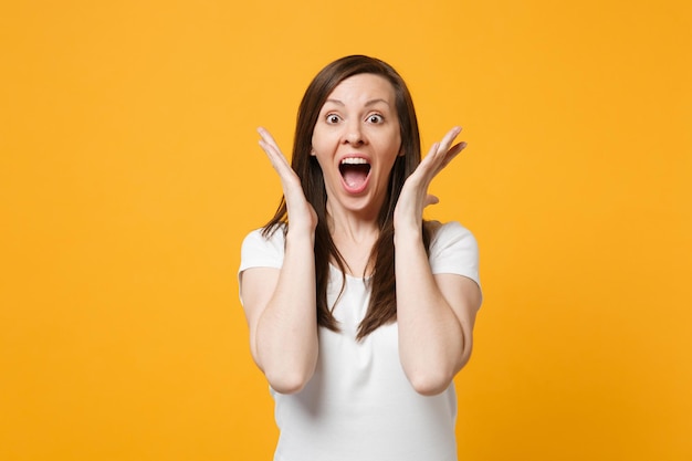 Retrato de una joven emocionada gritando con ropa blanca casual mirando la cámara, esparciendo las manos aisladas en un fondo naranja amarillo brillante en el estudio. Concepto de estilo de vida de las personas. Simulacros de espacio de copia.