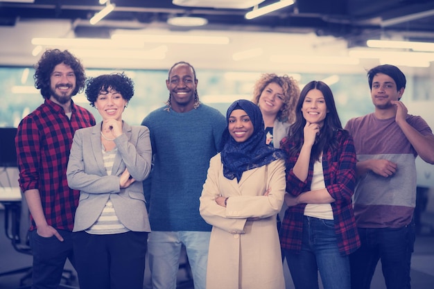 Retrato de joven emocionado equipo empresarial multiétnico de desarrolladores de software de pie y mirando a la cámara mientras celebra el éxito en la moderna oficina de inicio