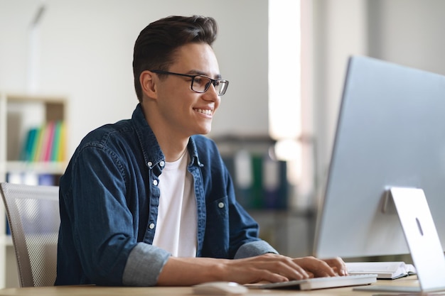 Retrato de un joven empleado de oficina sonriente trabajando en una laptop