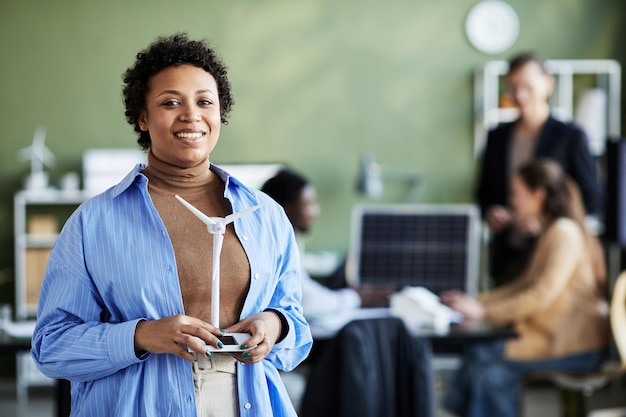 Retrato de una joven empresaria africana con maqueta de molino de viento sonriendo a la cámara mientras se reúne