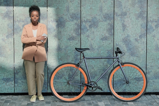 Retrato de joven empresaria africana en traje mirando a la cámara mientras está de pie al aire libre con bicicleta