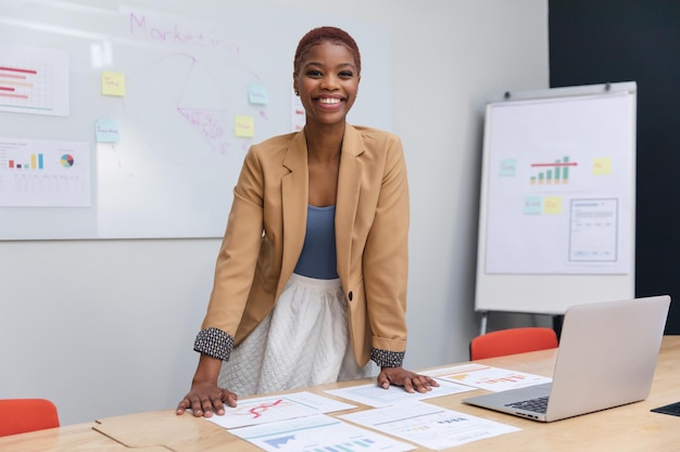 Retrato de una joven empresaria afroamericana sonriente con gráficos en la sala de juntas
