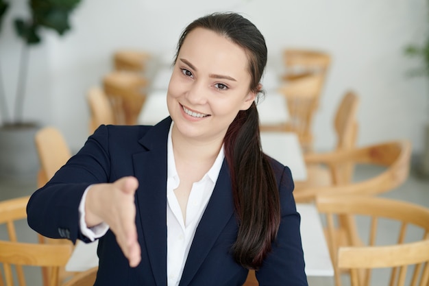 Retrato de joven empresaria alegre saludo socio comercial y brazo extendido para apretón de manos