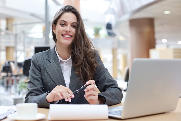 Retrato de una joven empresaria alegre sentado a la mesa en la oficina y mirando a la cámara.