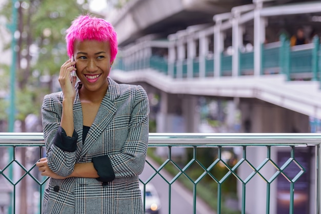 Retrato de joven empresaria asiática rebelde con cabello rosado en la pasarela en la ciudad al aire libre