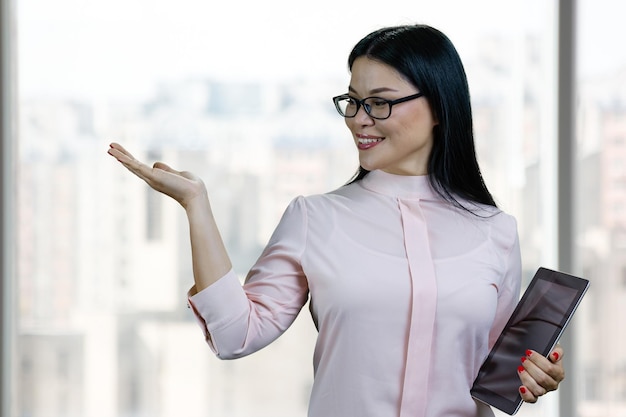 Foto retrato de una joven empresaria asiática sosteniendo una tableta y mostrando espacio de copia