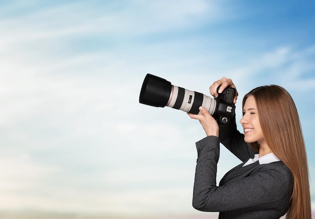 Retrato de una joven empresaria con cámara sobre fondo de cielo