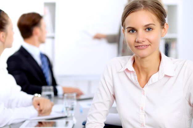 Retrato de una joven empresaria contra un grupo de empresarios en una reunión.