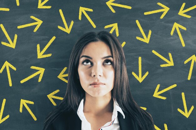 Foto retrato de una joven empresaria europea pensativa de pie en una pizarra con muchas flechas en el fondo concepto de dirección y decisión diferente