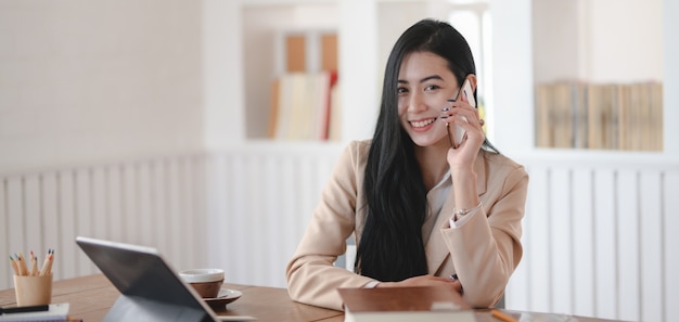 Retrato de joven empresaria hablando por teléfono con el cliente mientras sonríe a la cámara