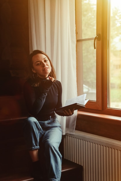 Retrato de joven empresaria con portátil y teléfono en la ventana del salón en casa de campo. Mujer adicta al trabajo en ropa casual de casa trabajando en vacaciones. Inspiración creativa y negocios