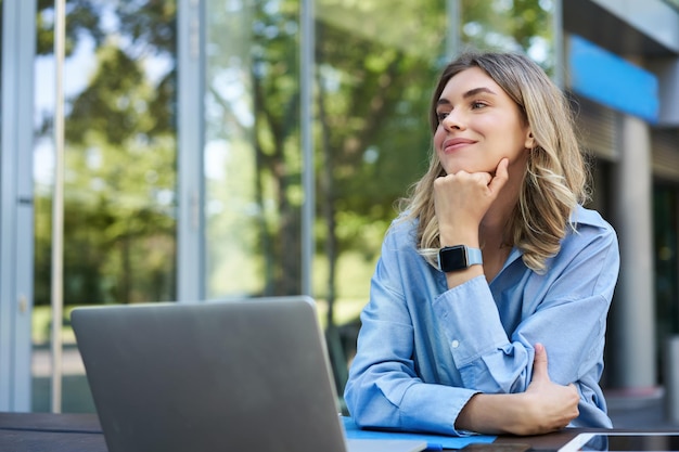 Retrato de una joven empresaria que trabaja al aire libre freelancer sonriendo sentada con una laptop fuera de bu